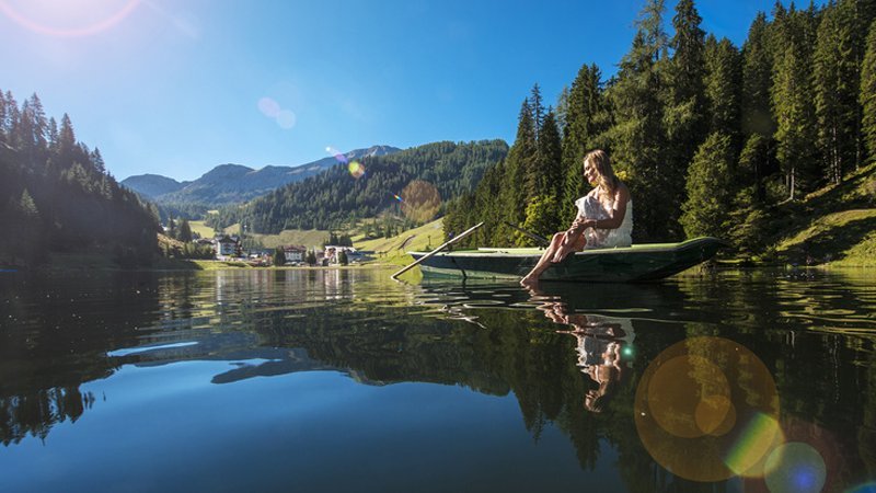 Eine Frau rudert auf einem See an einem Wald entlang