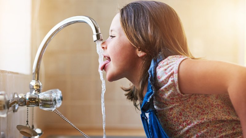 Ein Mädchen trinkt direkt aus dem Wasserhahn.
