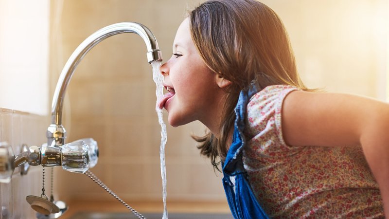 Ein Mädchen trinkt direkt aus dem Wasserhahn.