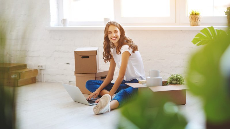 Eine junge Frau sitzt auf dem Boden ihrer ersten Wohnung
