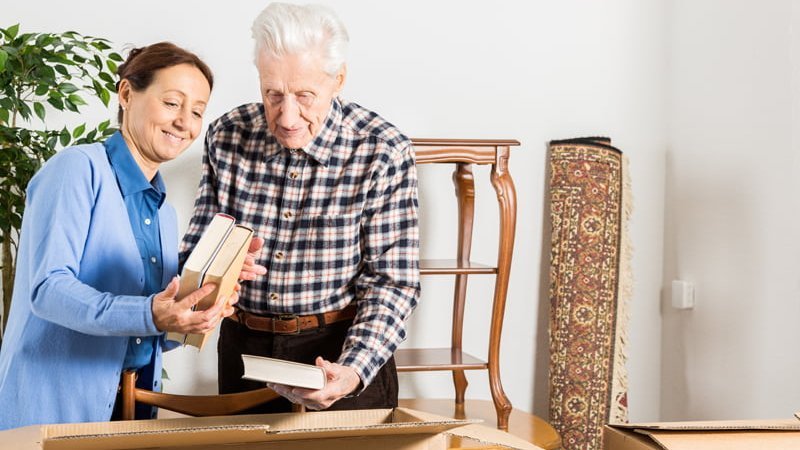 Haushaltsauflösung, Aussortieren, Entrümpeln, Frau packt mit älterem Mann Bücher in einen Karton