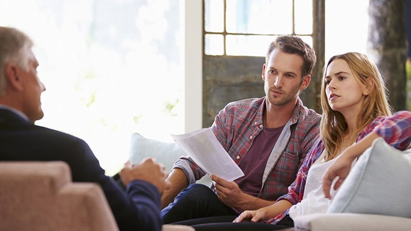 Ein Paar sitzt einem Mann gegenüber mit Unterlagen in den Händen