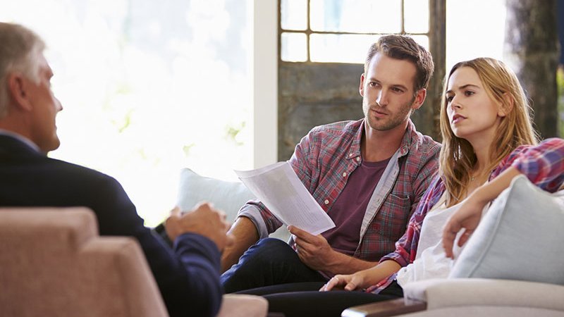 Ein Paar sitzt einem Mann gegenüber mit Unterlagen in den Händen